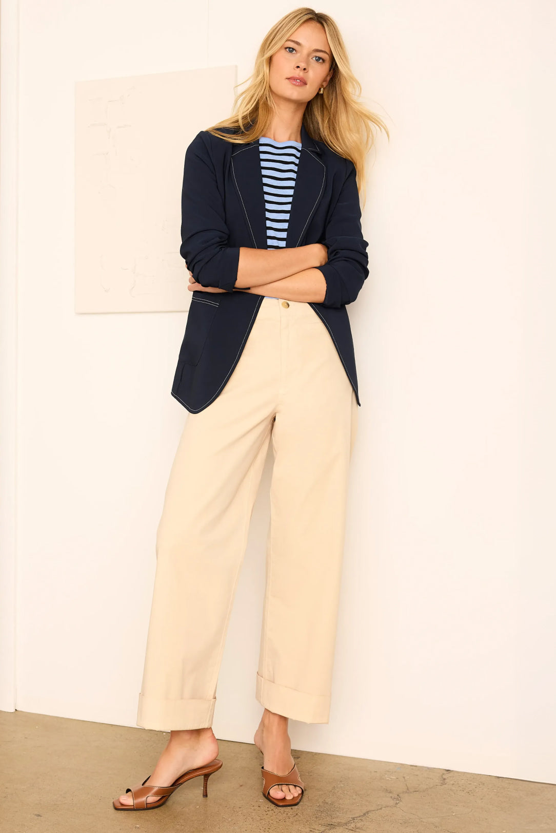Woman wearing a navy blazer, striped shirt, and beige pants against a plain background