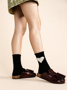 Black crew socks featuring a white knitted heart design on the outer ankle.
