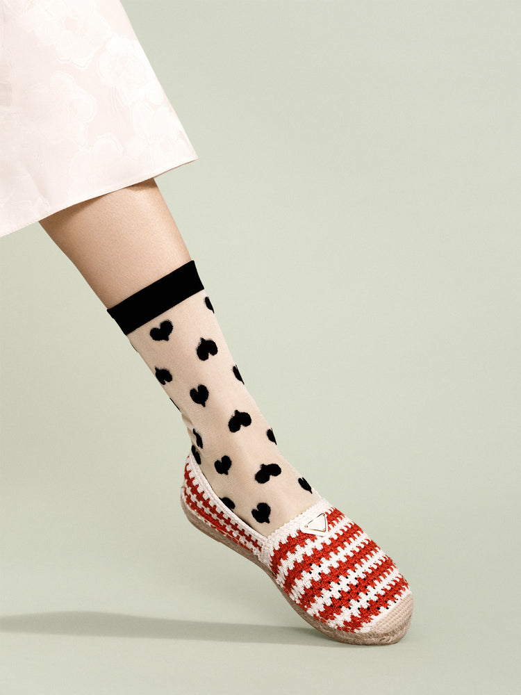 Red and white crochet espadrilles are worn with sheer nude ankle socks featuring an allover black heart print and cuff.