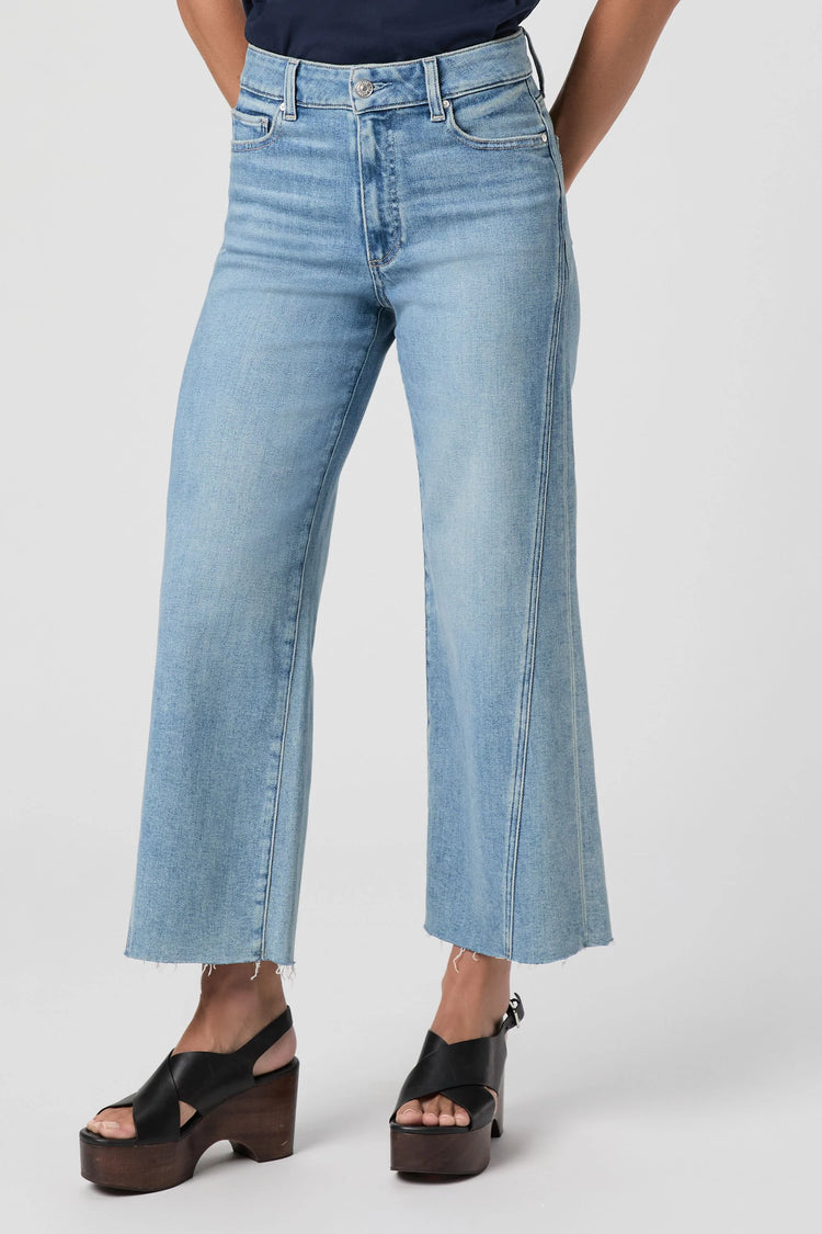 Light wash blue high-waisted wide-leg jeans with a twisted outseam panel and frayed raw hems.