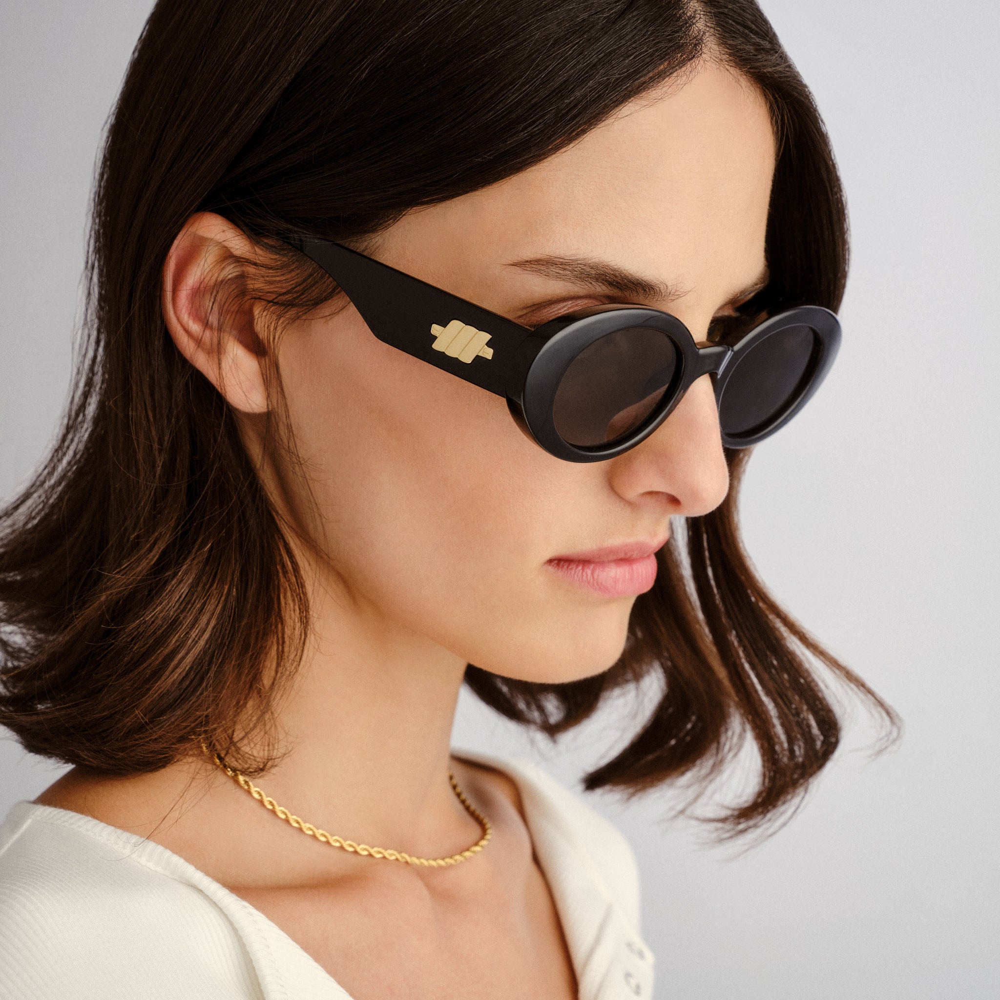 Model wears chunky black oval sunglasses with gold hardware for a sleek and retro-inspired fit.