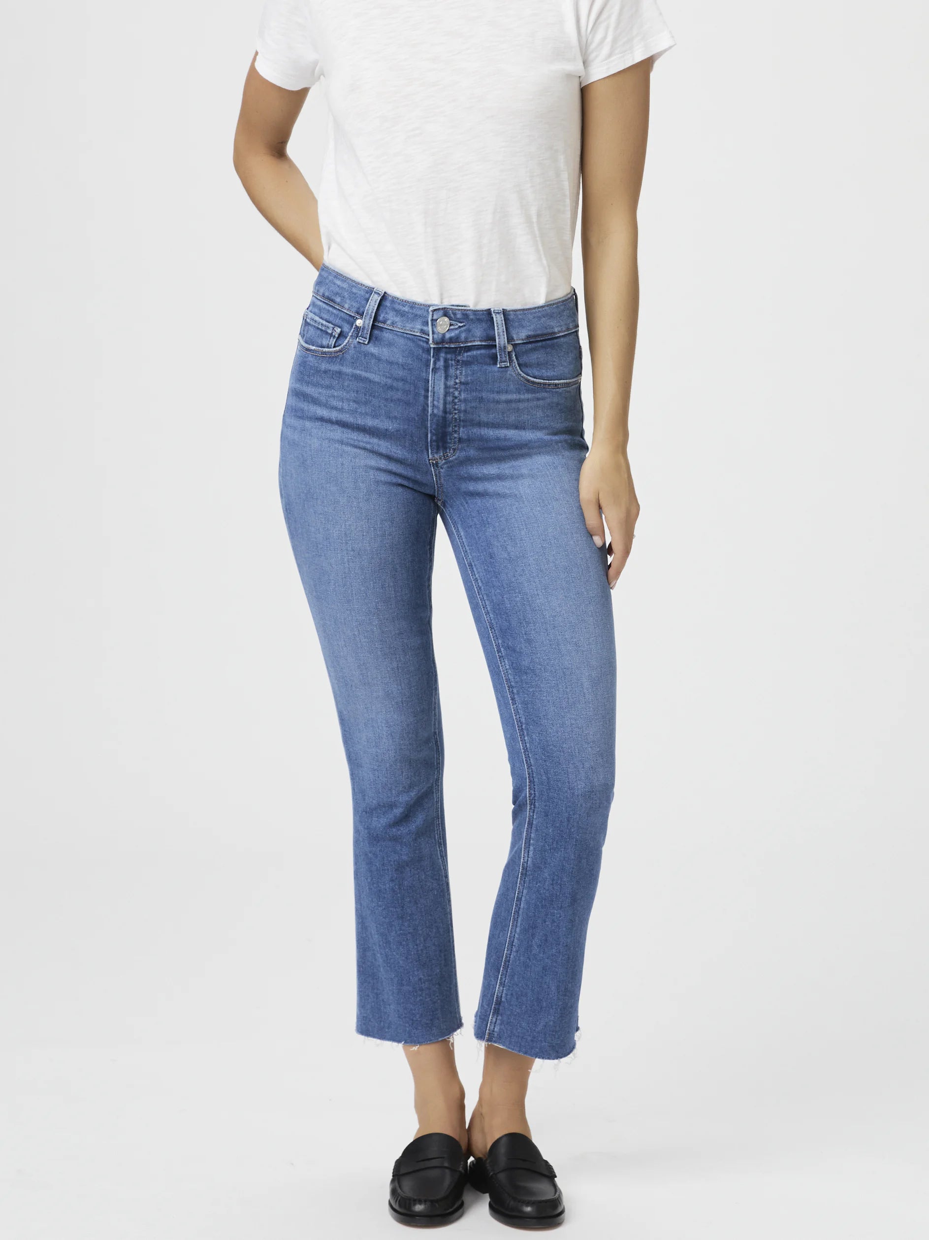 Mid-rise, light-wash blue cropped flare jeans with a raw hem. Model wears black loafers.