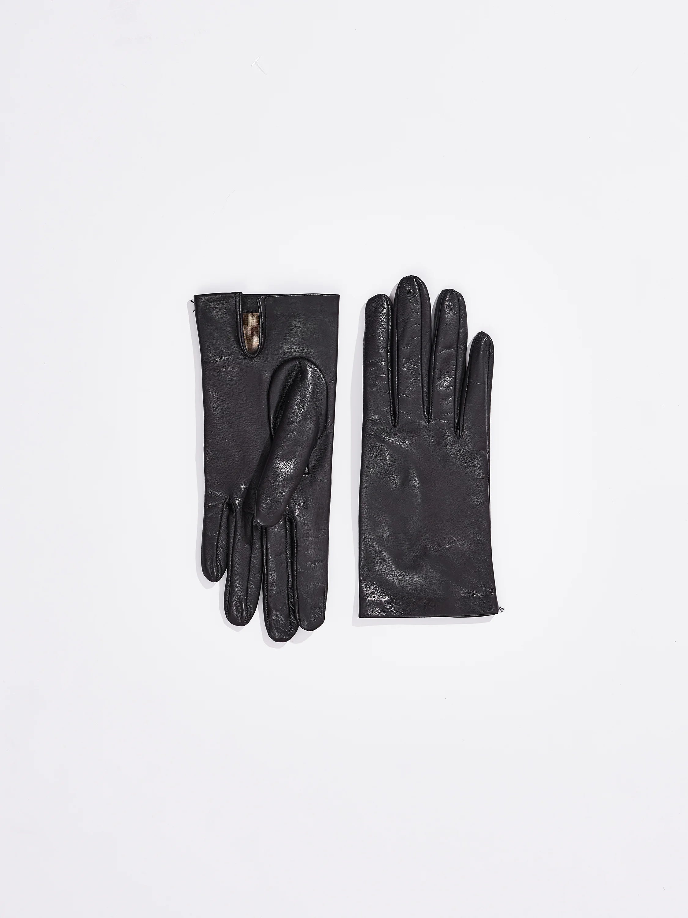 A pair of black lambskin gloves on a white background. One glove shows a short wrist opening with a tan lining.