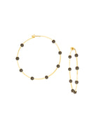 A pair of thin gold hoop earrings with dark, round gems spaced along each hoop.