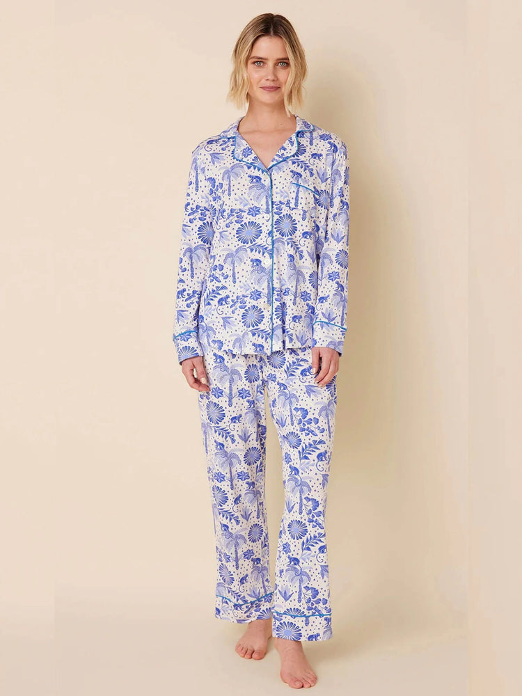 White pajama set with blue monkey, palm tree, and floral print. Button-front long-sleeve top, long pants, blue piping.