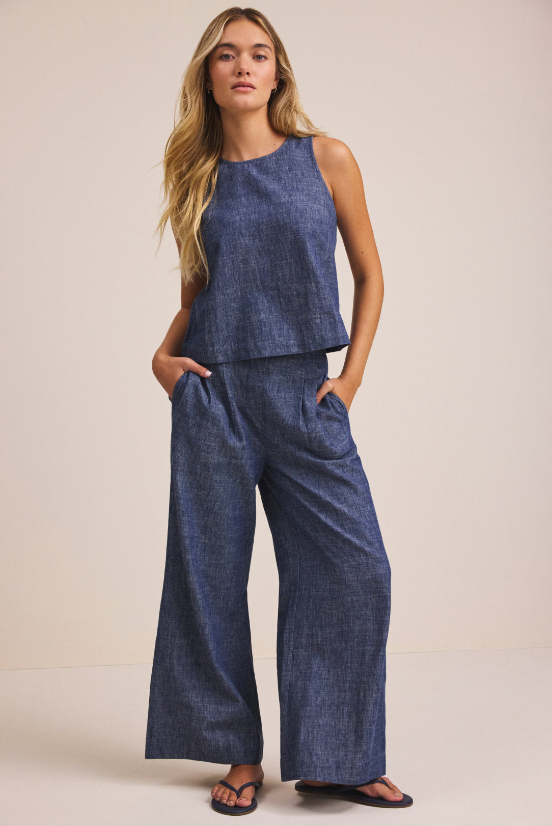 Woman wearing a blue sleeveless top and wide-leg pants against a beige background
