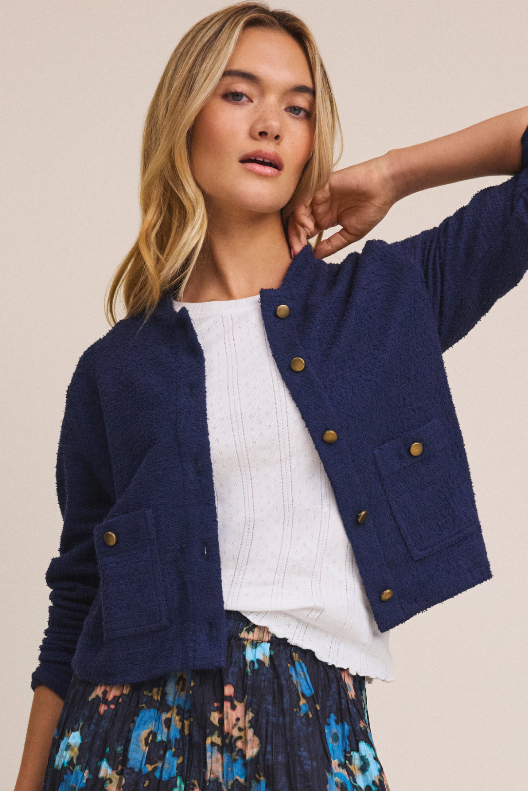 Woman wearing a navy blue cardigan over a white top with a floral skirt on a beige background