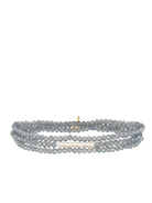 Multi-strand stretch bracelet: faceted blue-grey beads, horizontal off-white baroque pearl, small gold accent.