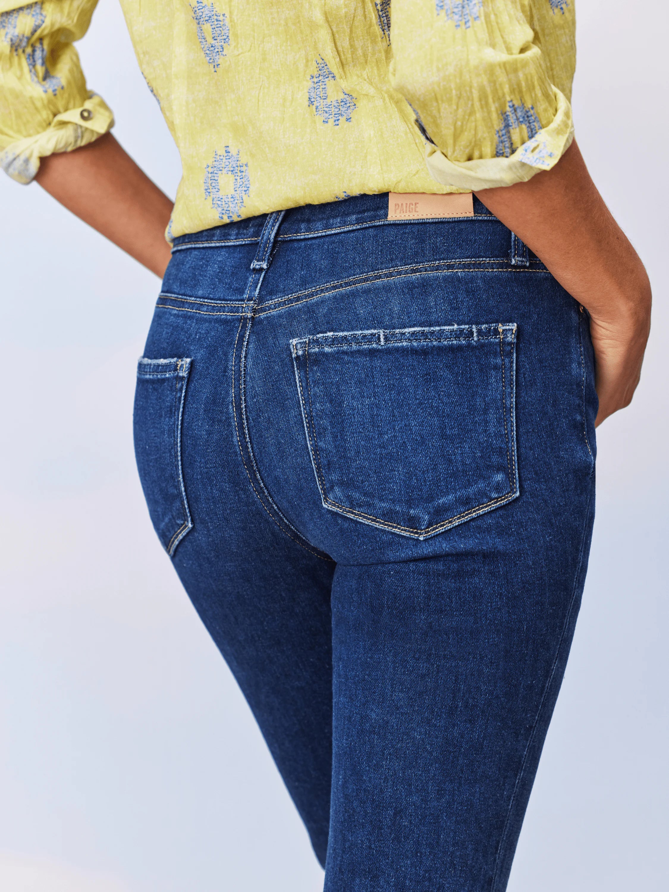 Dark wash blue jeans shown from the back; raw hem; small Paige leather label.