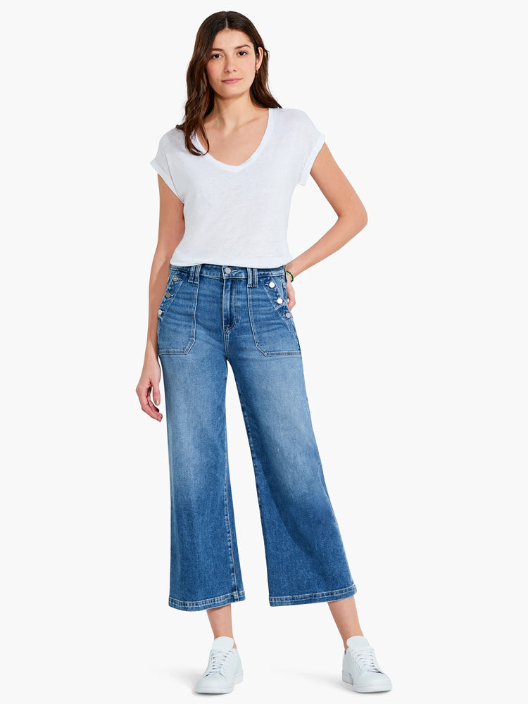 Mid-wash blue, wide-leg cropped jeans. Features multiple front pockets and silver buttons. Model wears white top and shoes.