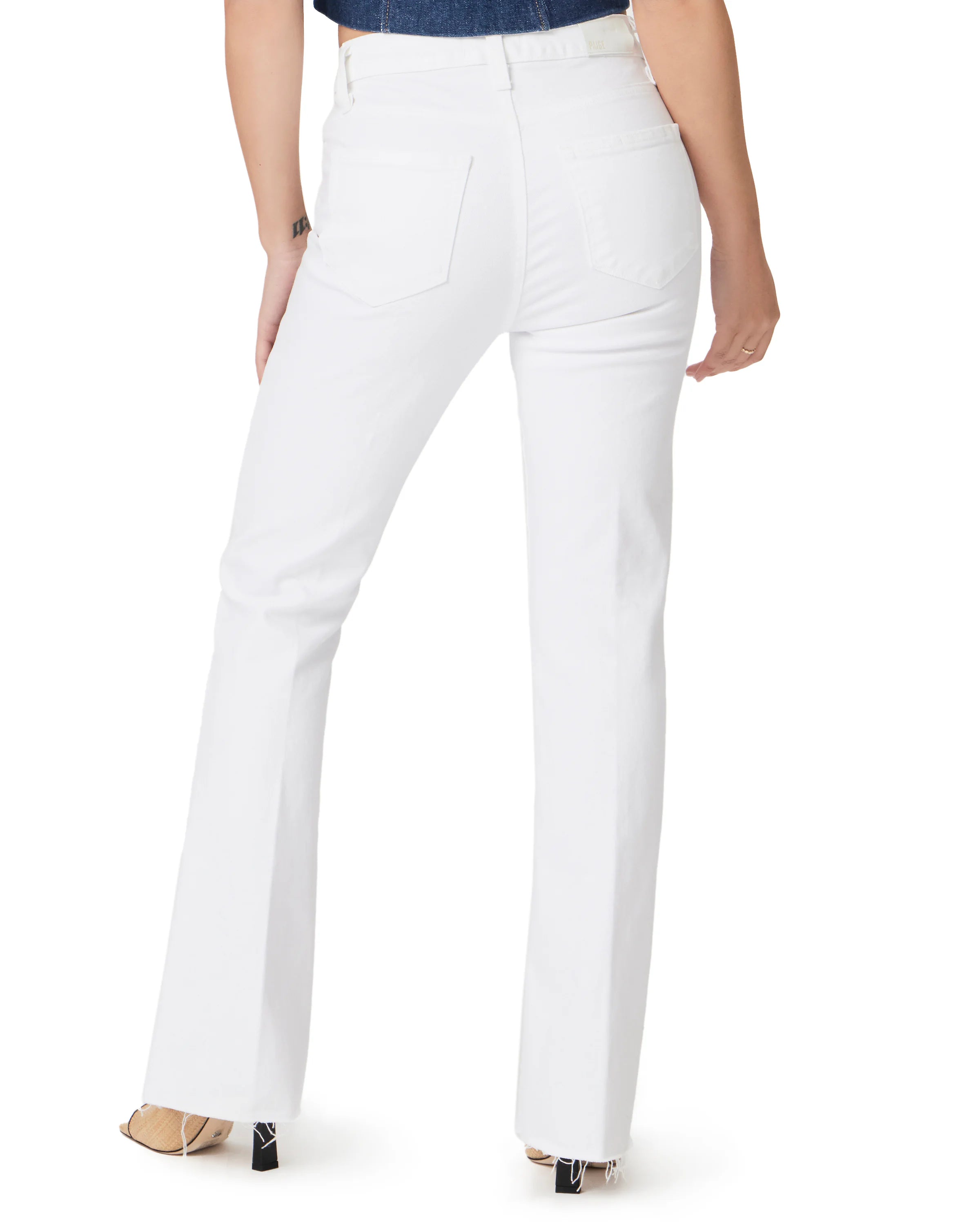 White high-rise bootcut jeans, seen from the back, with back pockets, a Paige tag, and frayed hems.