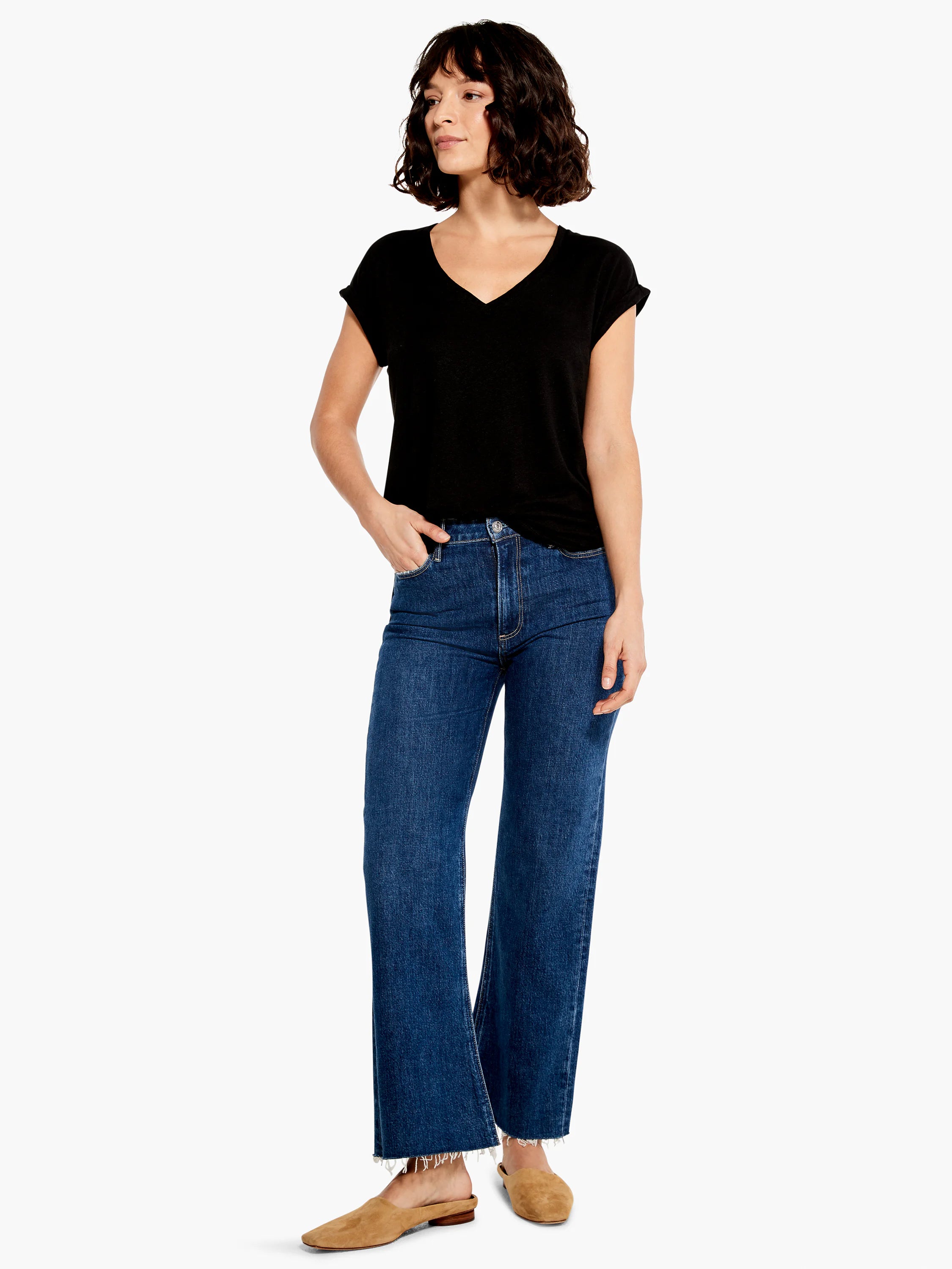 Dark wash blue, wide-leg ankle jeans with frayed hems; model wears a black v-neck top and tan shoes.