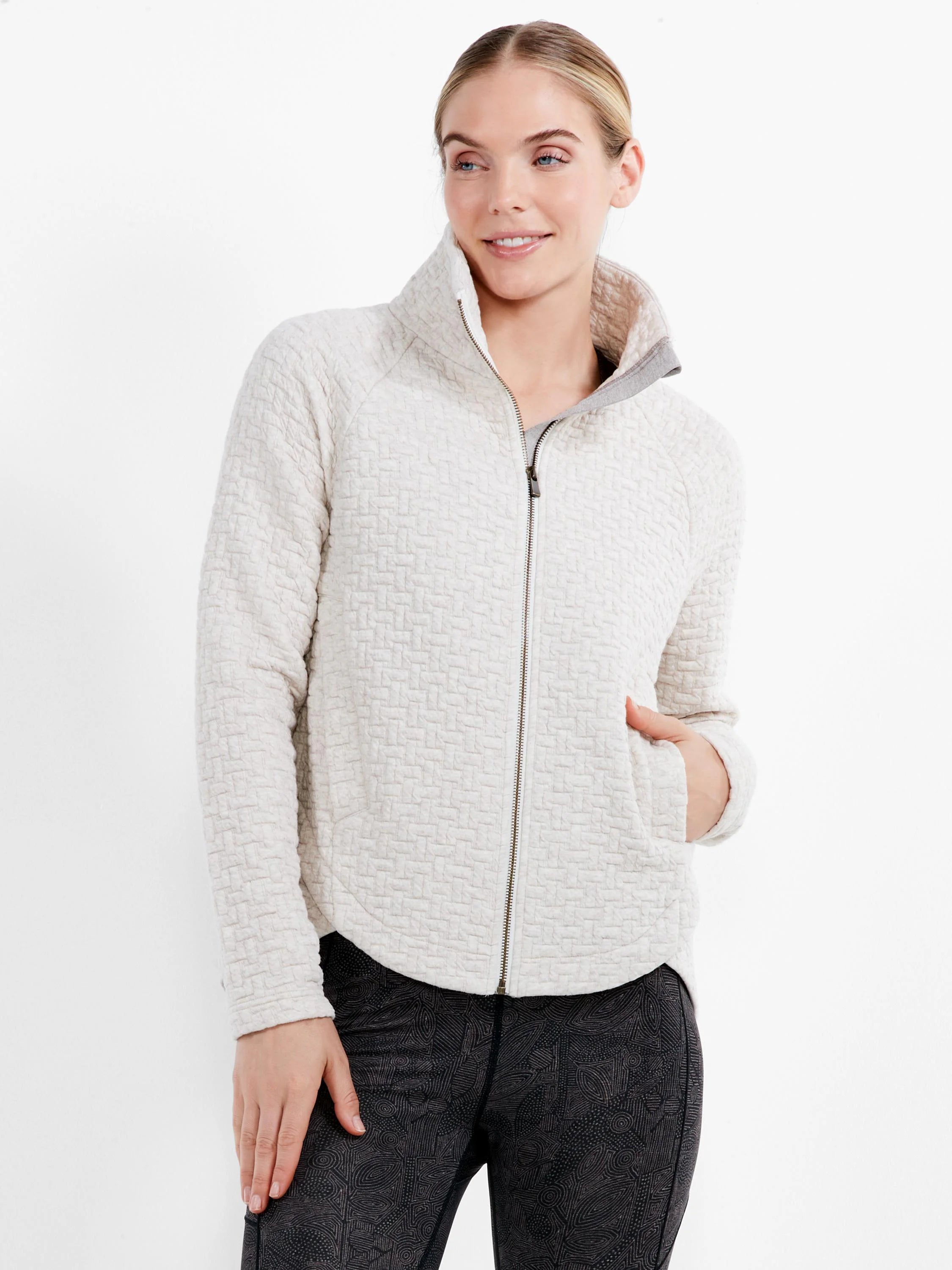 Woman wears a light cream quilted jacket with a basketweave pattern, stand collar, and full zipper closure.
