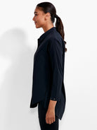 Black collared shirt with long sleeves, snaps on sleeves, and a rounded high-low hem, worn by a model.