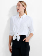 White collared button-down shirt. Bottom tied in a knot at the waist. Rolled sleeves show dark cuff buttons.