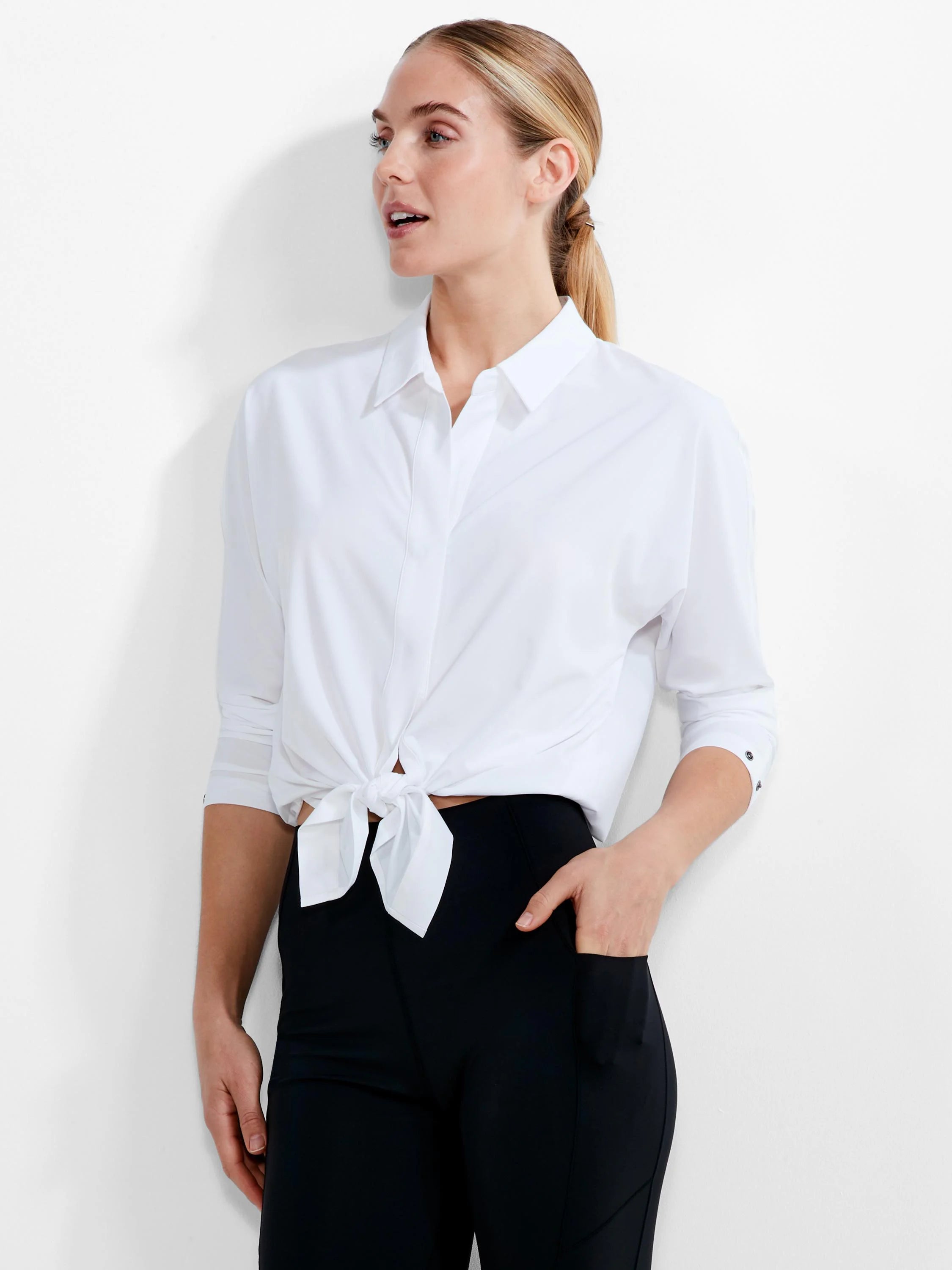 White collared button-down shirt. Bottom tied in a knot at the waist. Rolled sleeves show dark cuff buttons.