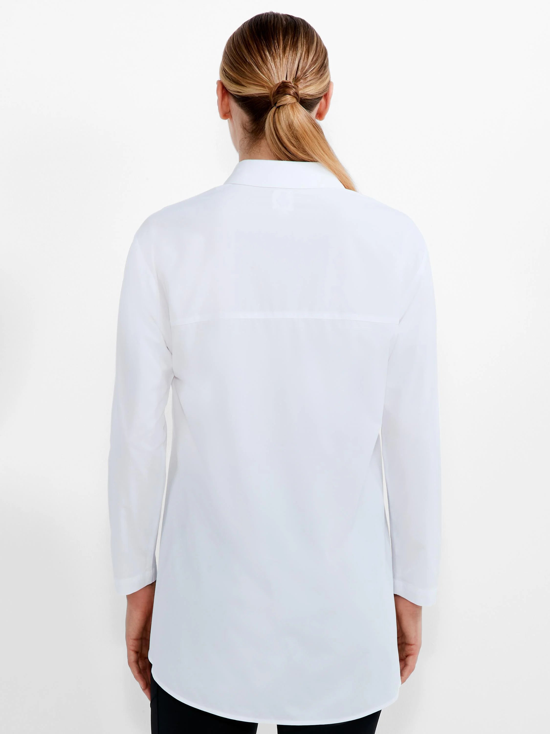 White long-sleeved shirt, back view on model. Features a collar, horizontal upper back seam, and curved hem.