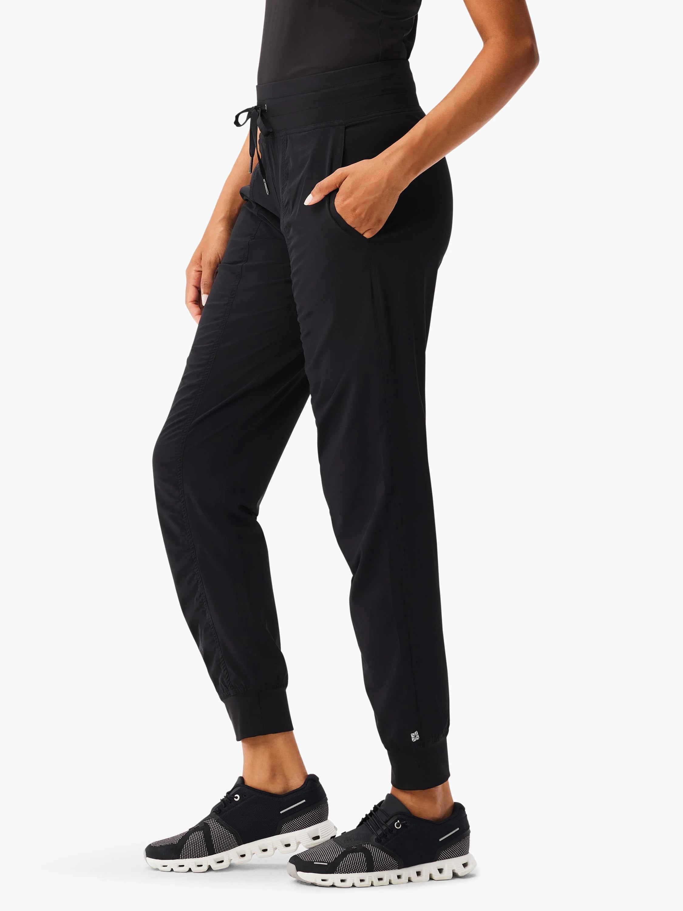 Black jogger pants with a drawstring waist, side pockets, tapered legs, subtle ruching, and cuffed ankles.
