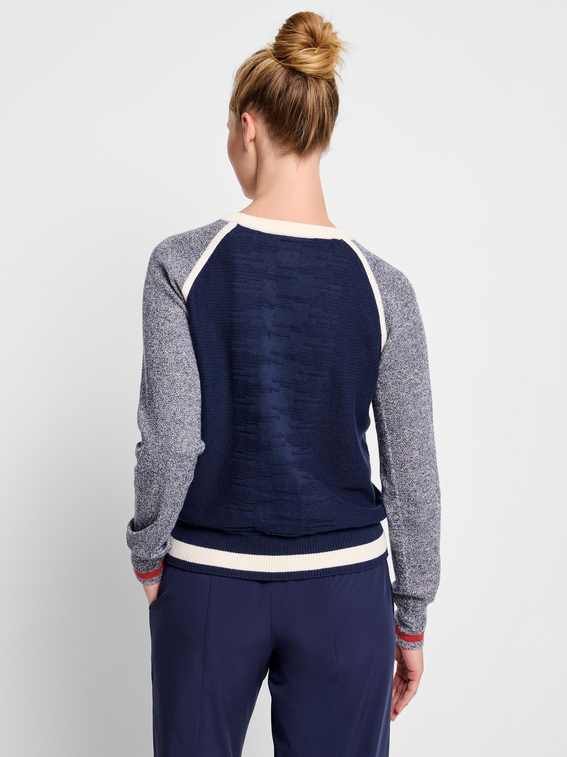Navy blue sweater with mottled gray sleeves and off-white/cream accents. Red stripes at cuffs and hem.