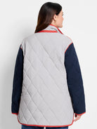 Back view of quilted coat: light grey body, navy sleeves, with coral piping on collar, cuffs, and hem.