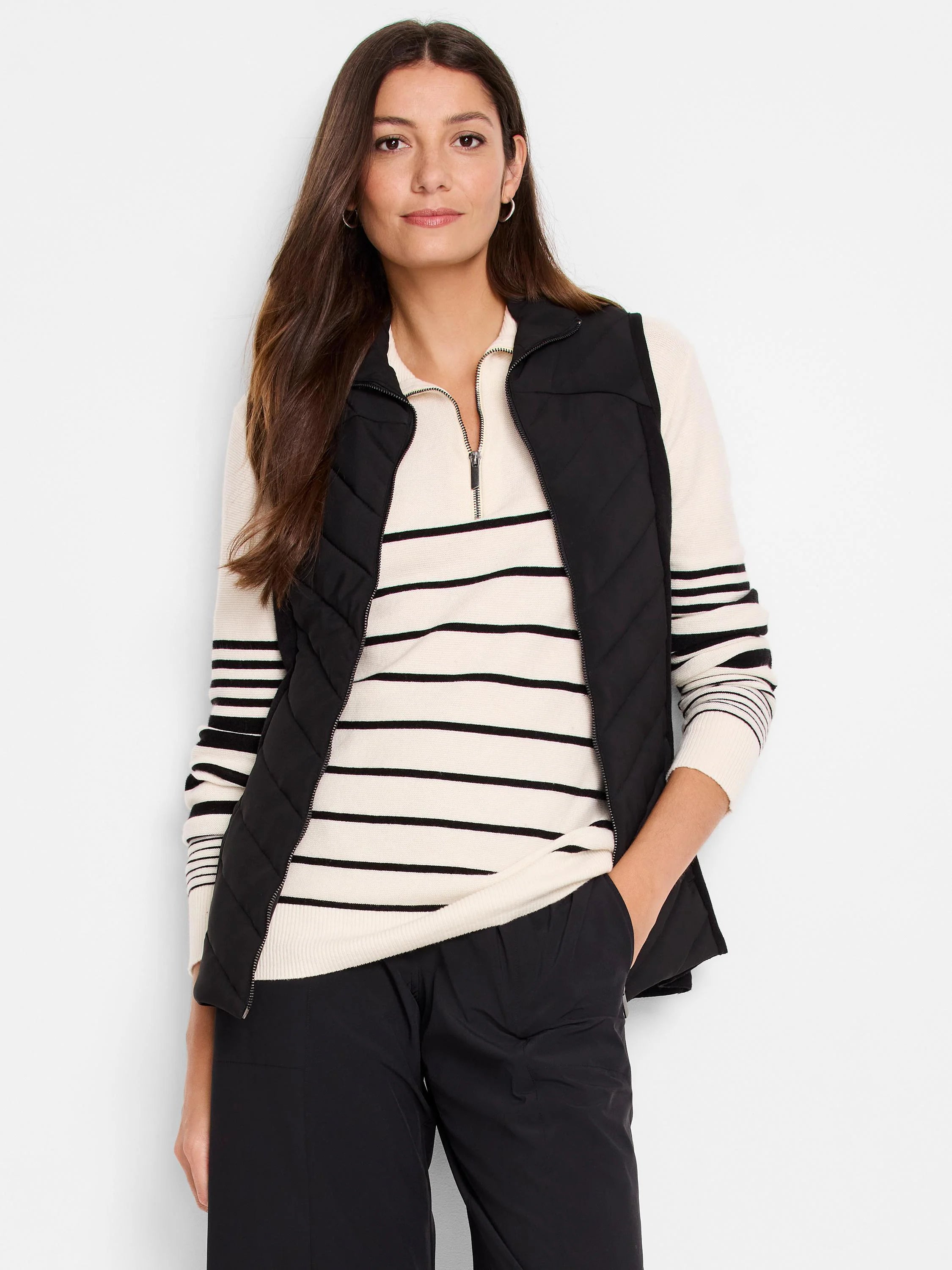 Black quilted puffer vest with a zipper. The model is wearing it over a cream and black striped sweater.