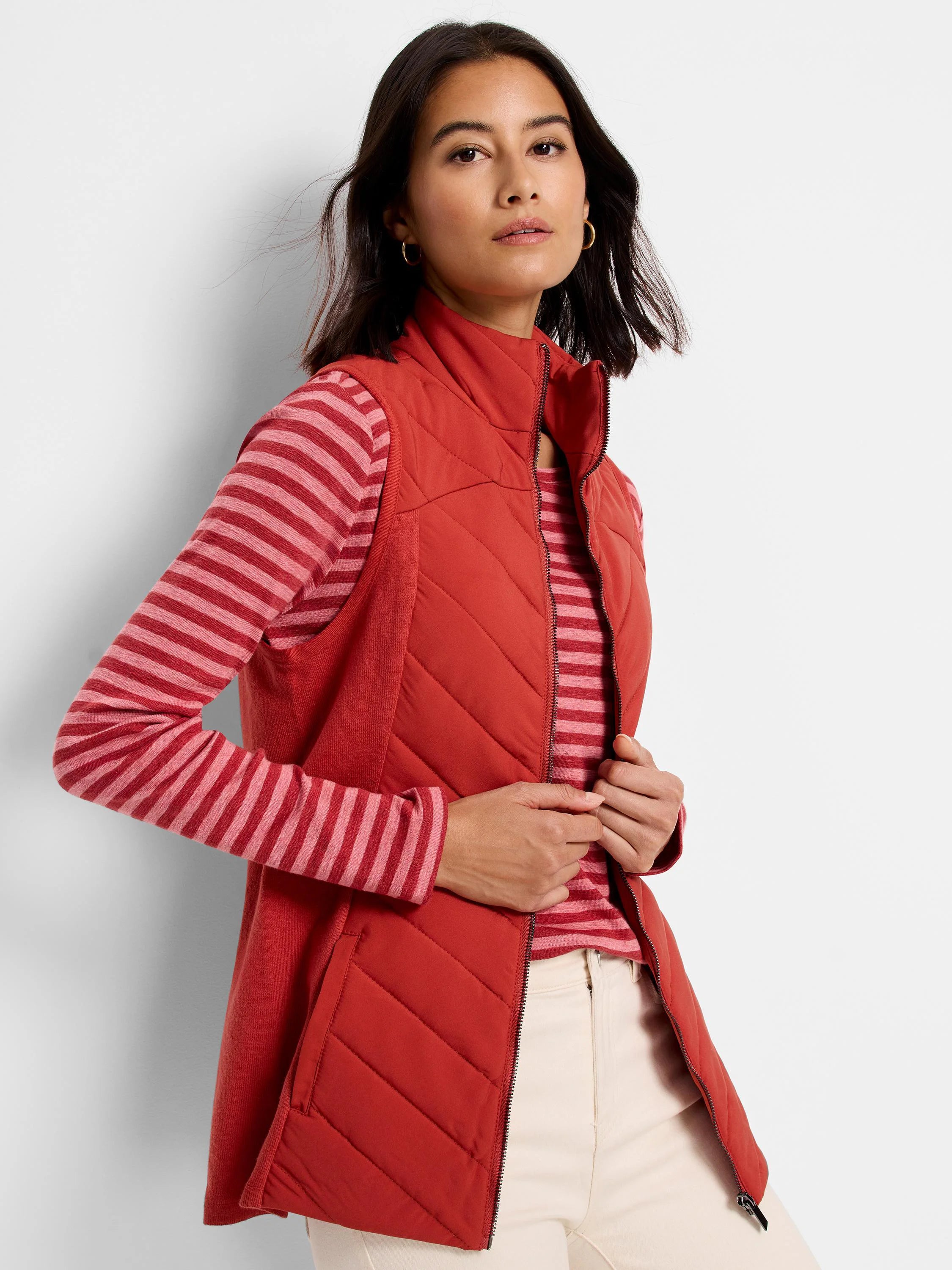 Red quilted puffer vest with knit trim, zipper closure. Model wears it over a pink and red striped shirt.