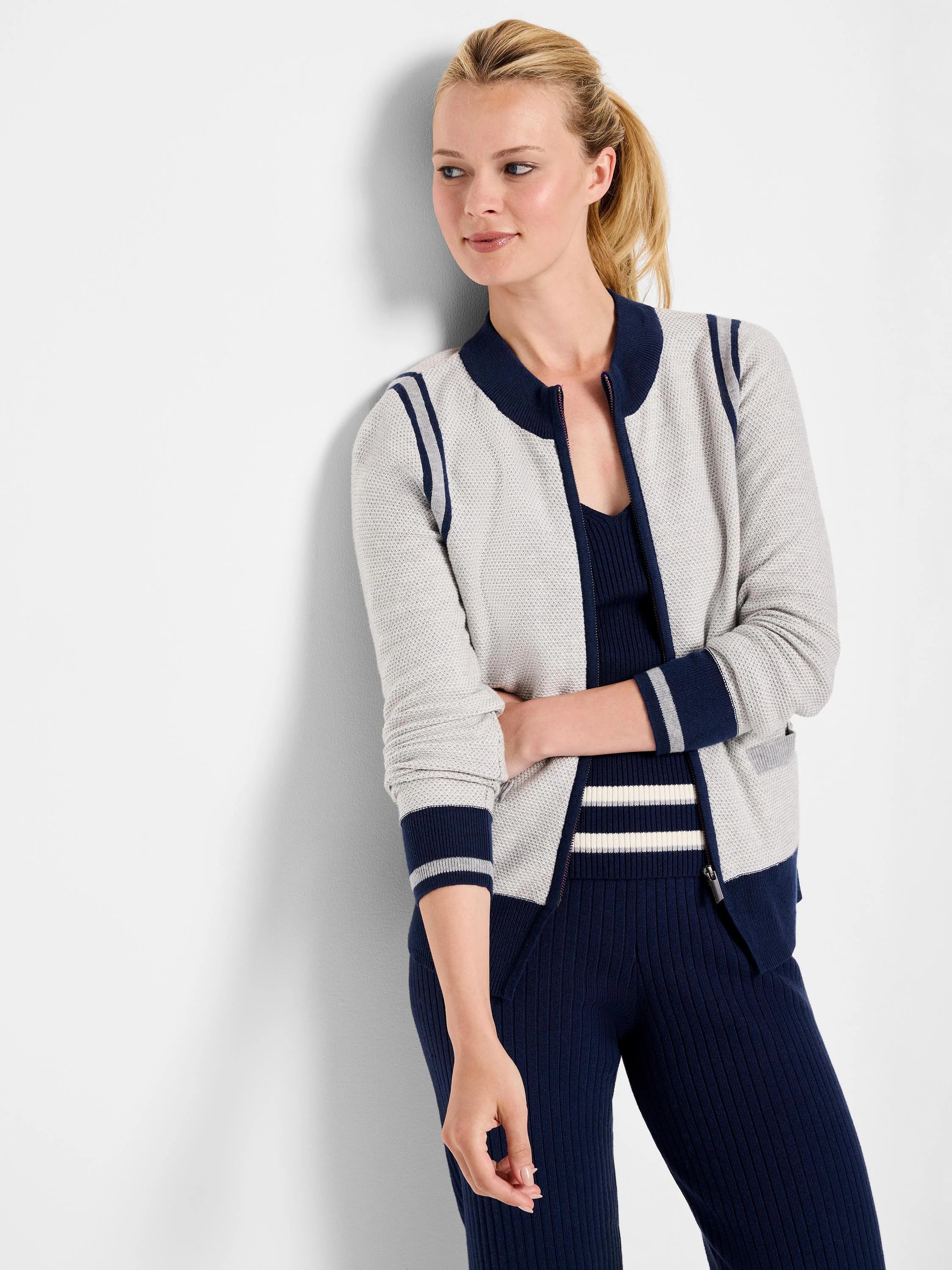 Gray zip-front cardigan with navy blue and white stripes on the sleeves and hem. The cardigan has a textured knit.