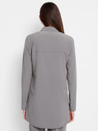 Back view of a woman wearing a grey, long-sleeved collared shirt with a relaxed fit and back yoke.