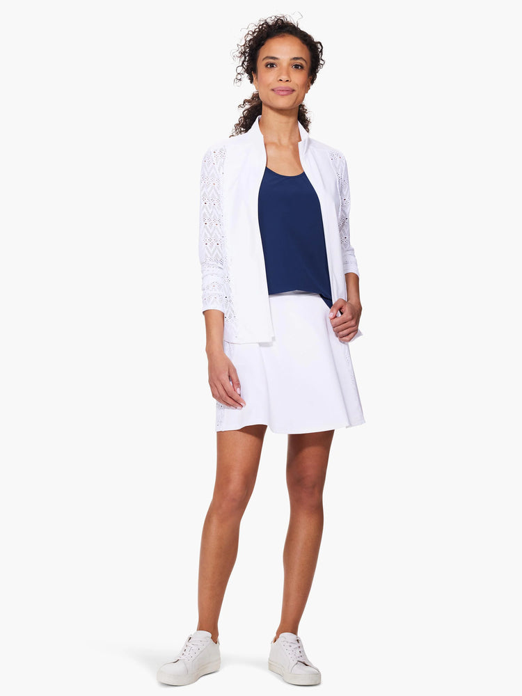 White jacket with lacy, geometric sleeves; zip front. Model also wears white skirt and shoes; navy top.
