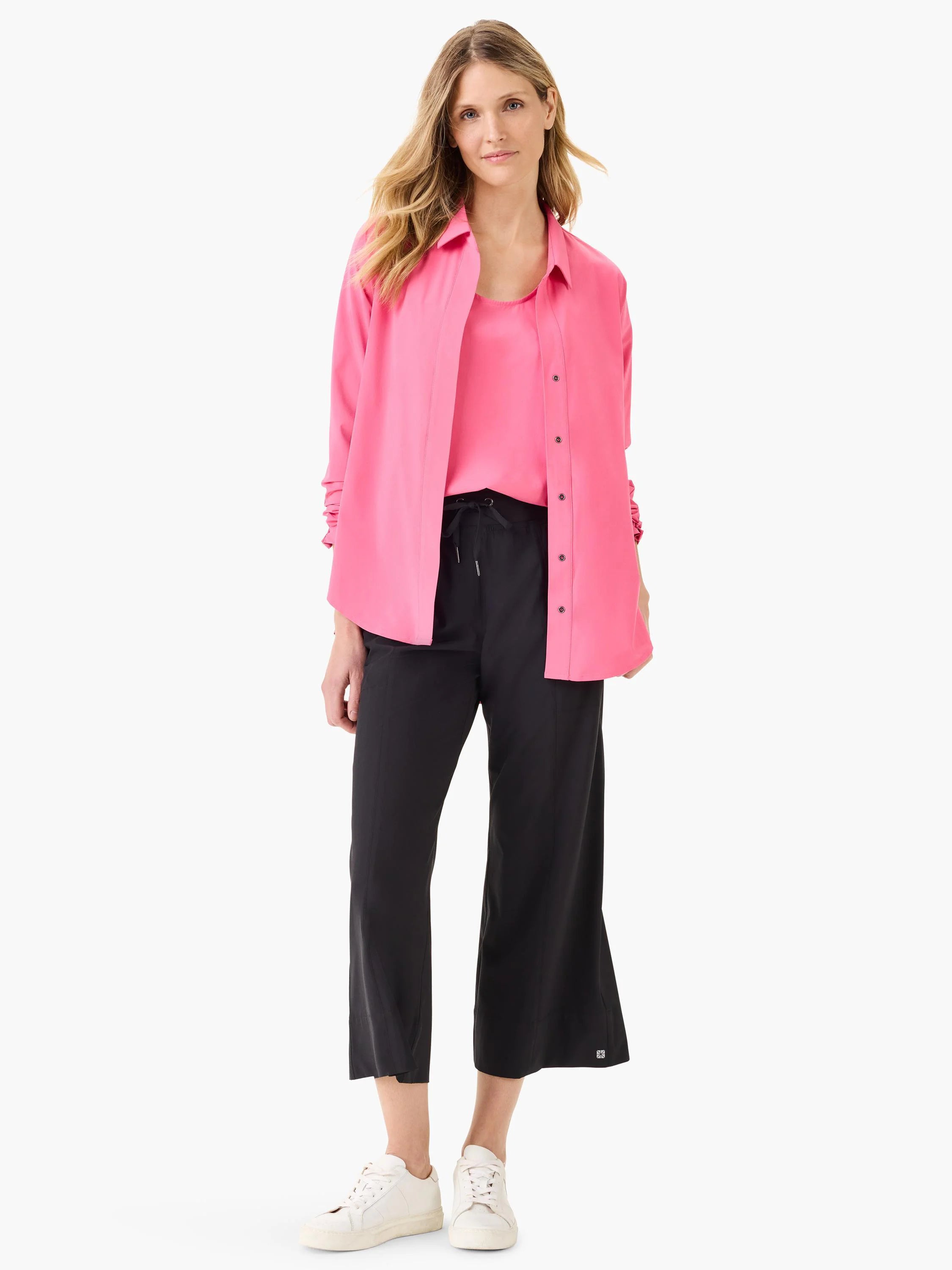 Hot pink tank top layered under a hot pink button-up shirt. Model also wears black cropped pants and white sneakers.