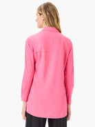 Bright pink long-sleeve collared shirt, relaxed fit, curved hem, worn by a model facing away.
