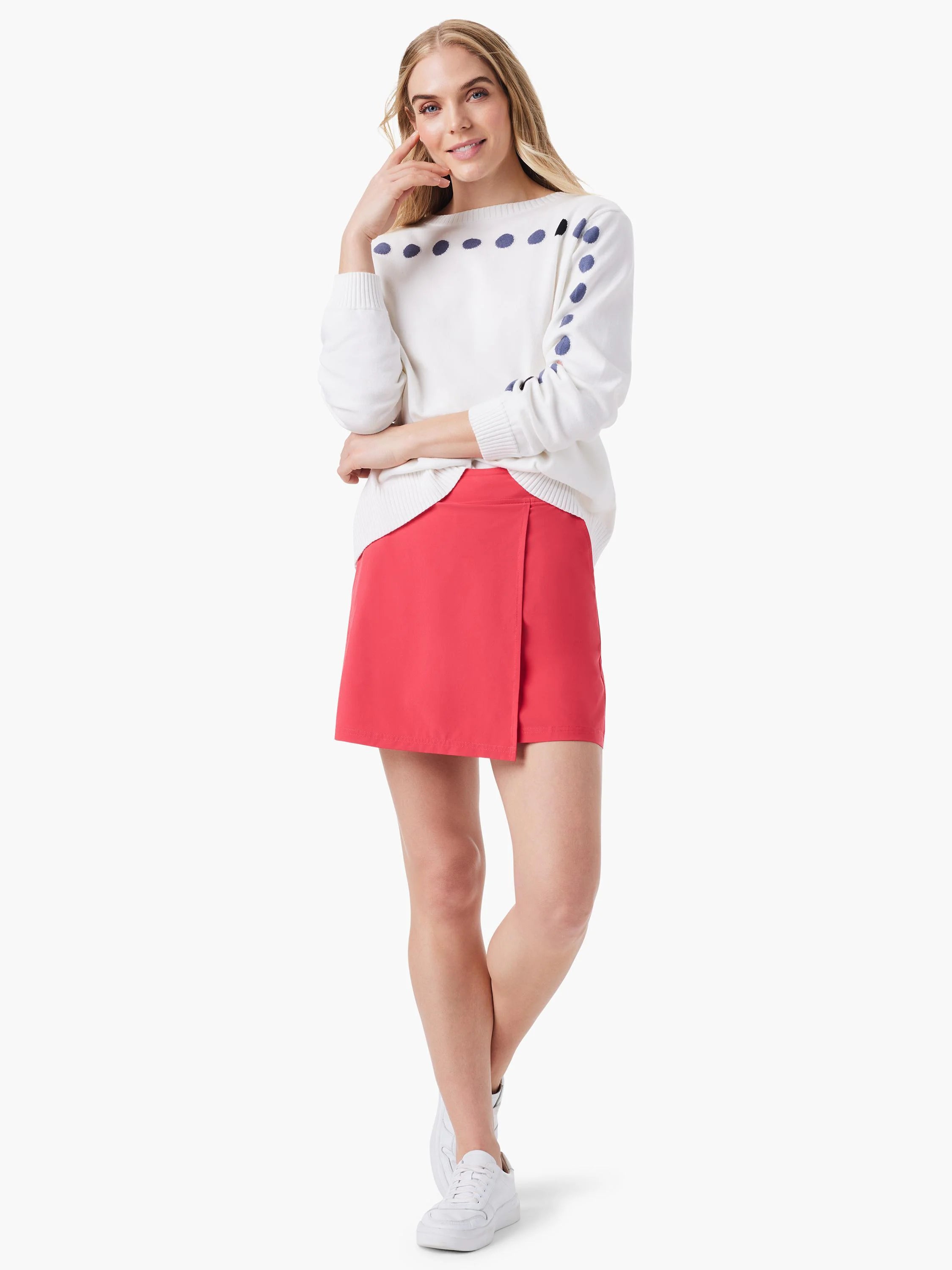 Off-white sweater with dark-blue dots, coral-pink skirt, and white sneakers.