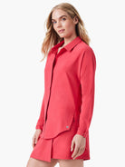 Coral long-sleeve collared shirt with an open neckline, side slits at the hem, and a small logo detail.