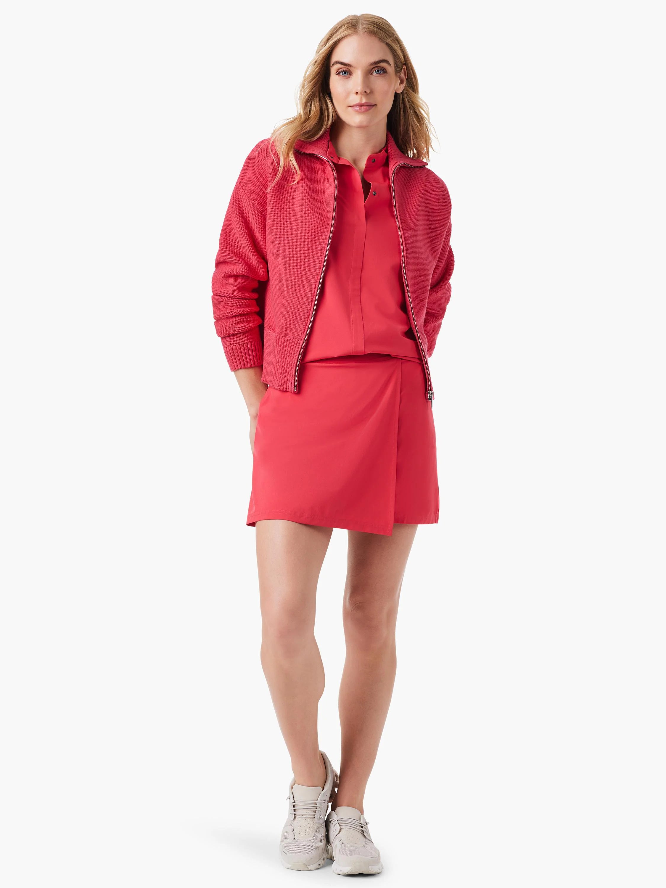 Coral pink skort and matching zip-up jacket.  Model wears light beige sneakers.