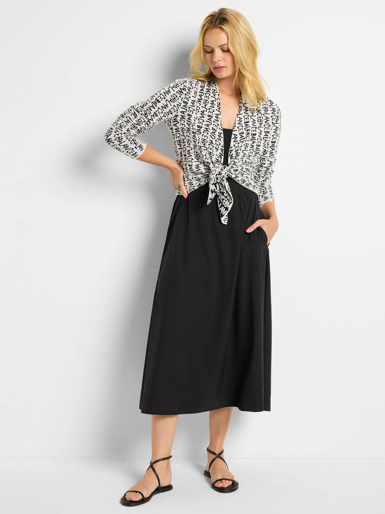 Off-white cardigan with black text print, tied at waist. Three-quarter sleeves. Shown with black midi skirt and sandals.