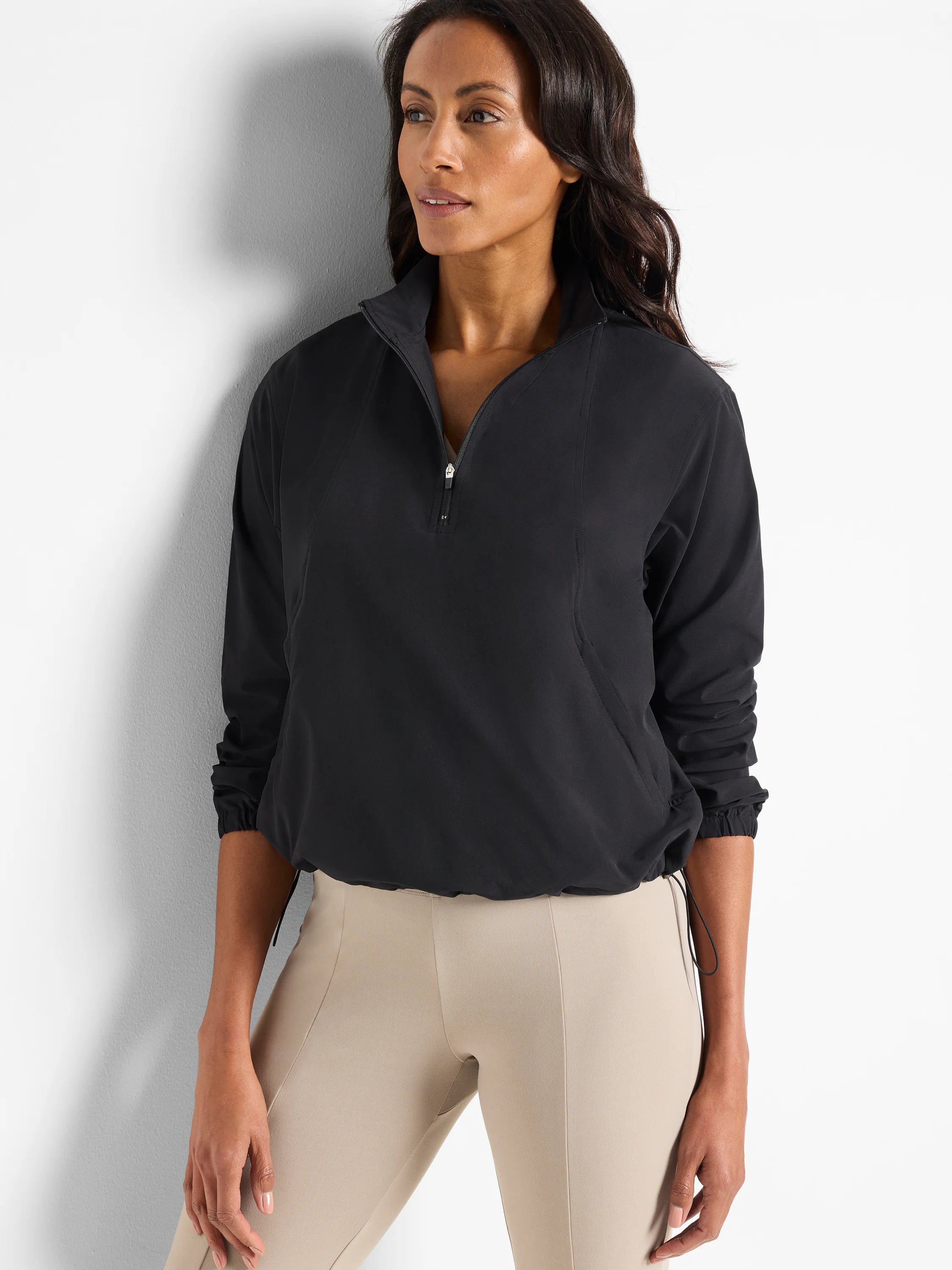 Black, half-zip pullover with long sleeves and drawstring hem. Model also wearing light beige pants.