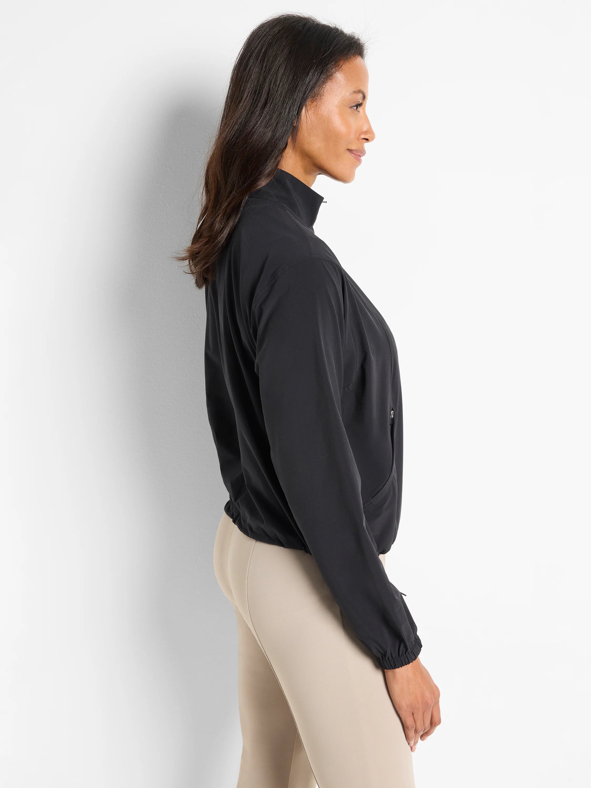 Black popover with long sleeves and elastic cuffs. Side zip pocket detail. Model wears beige pants.