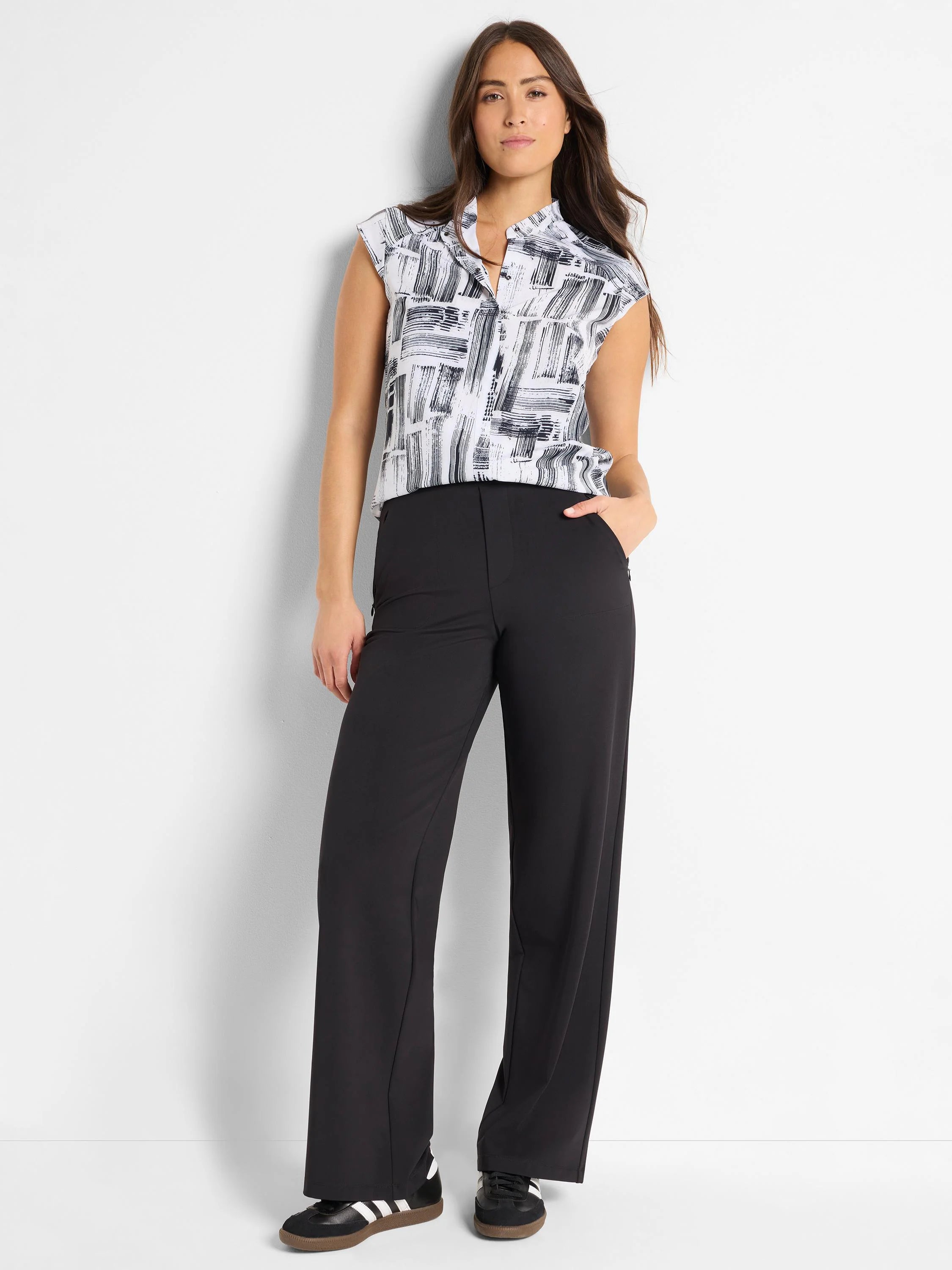 White sleeveless top with black abstract print, black wide-leg pants, black and white sneakers.