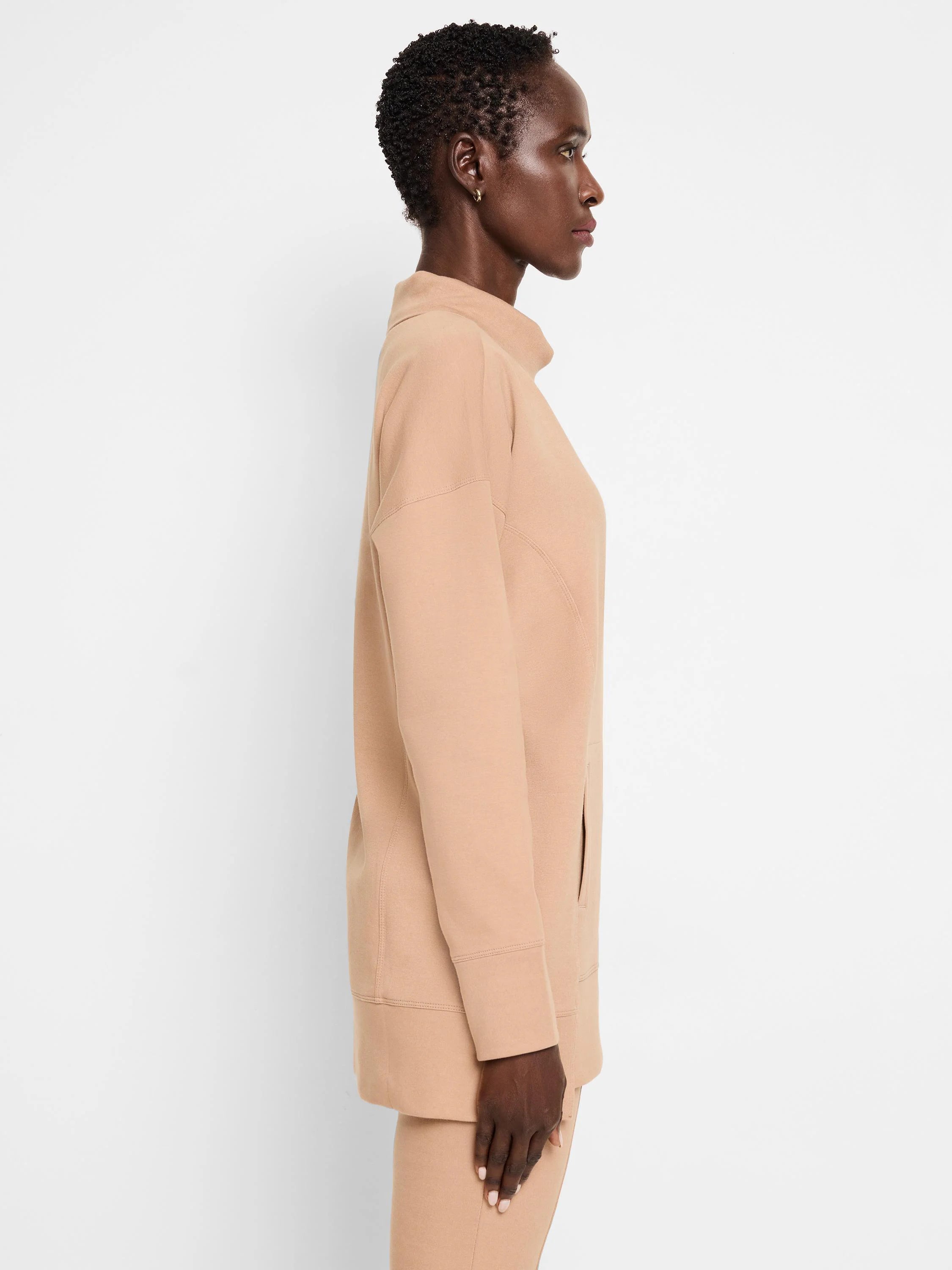 Beige tunic with funnel neck, long sleeves, and a side pocket. Seams are visible.