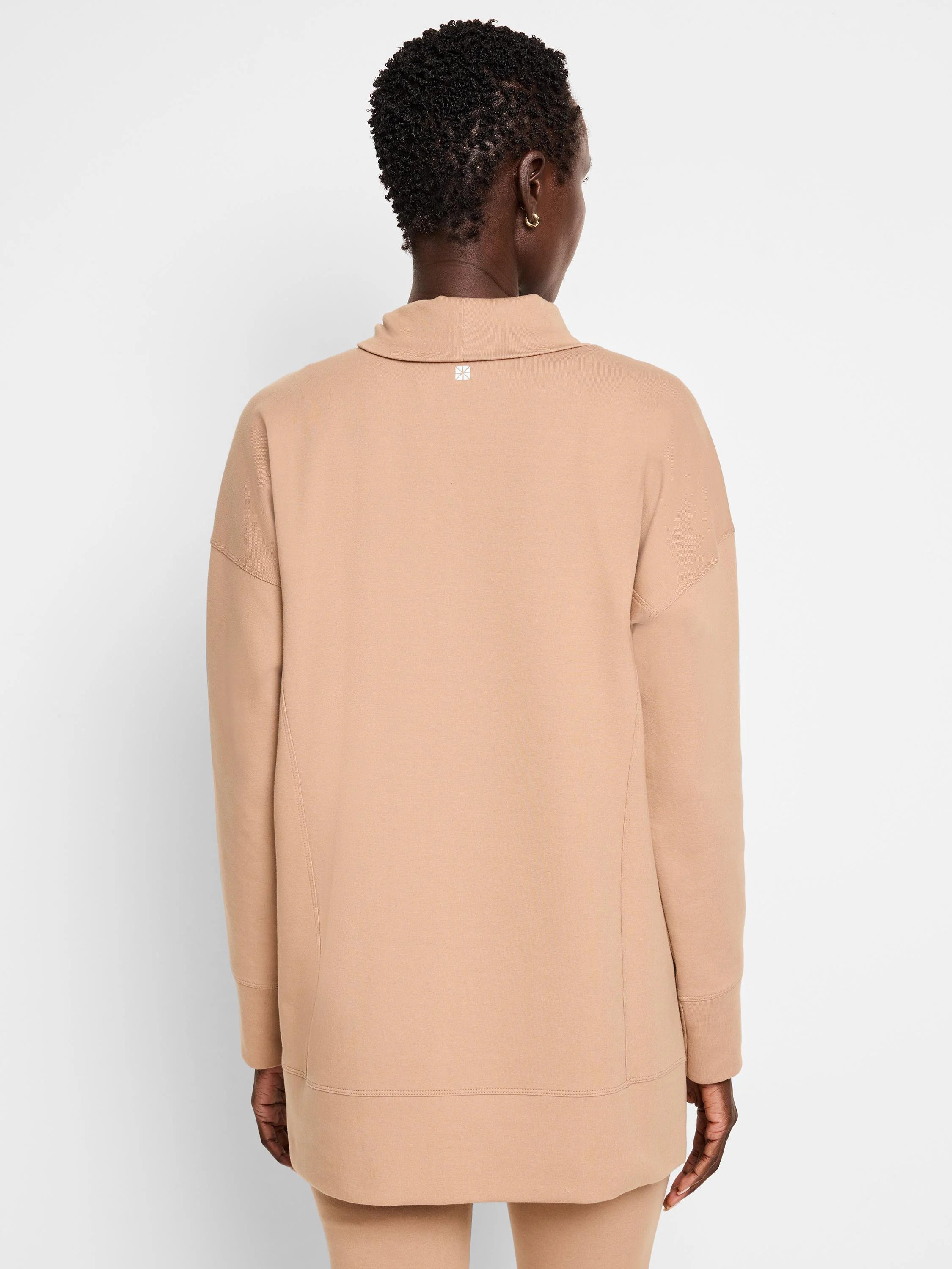 Beige tunic, long sleeves, funnel neck. Seams visible at shoulders and hem. Small logo on back.