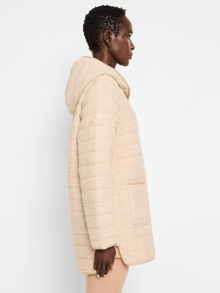 Beige quilted hooded coat with lighter beige trim. Horizontal quilting detail. Side profile view.