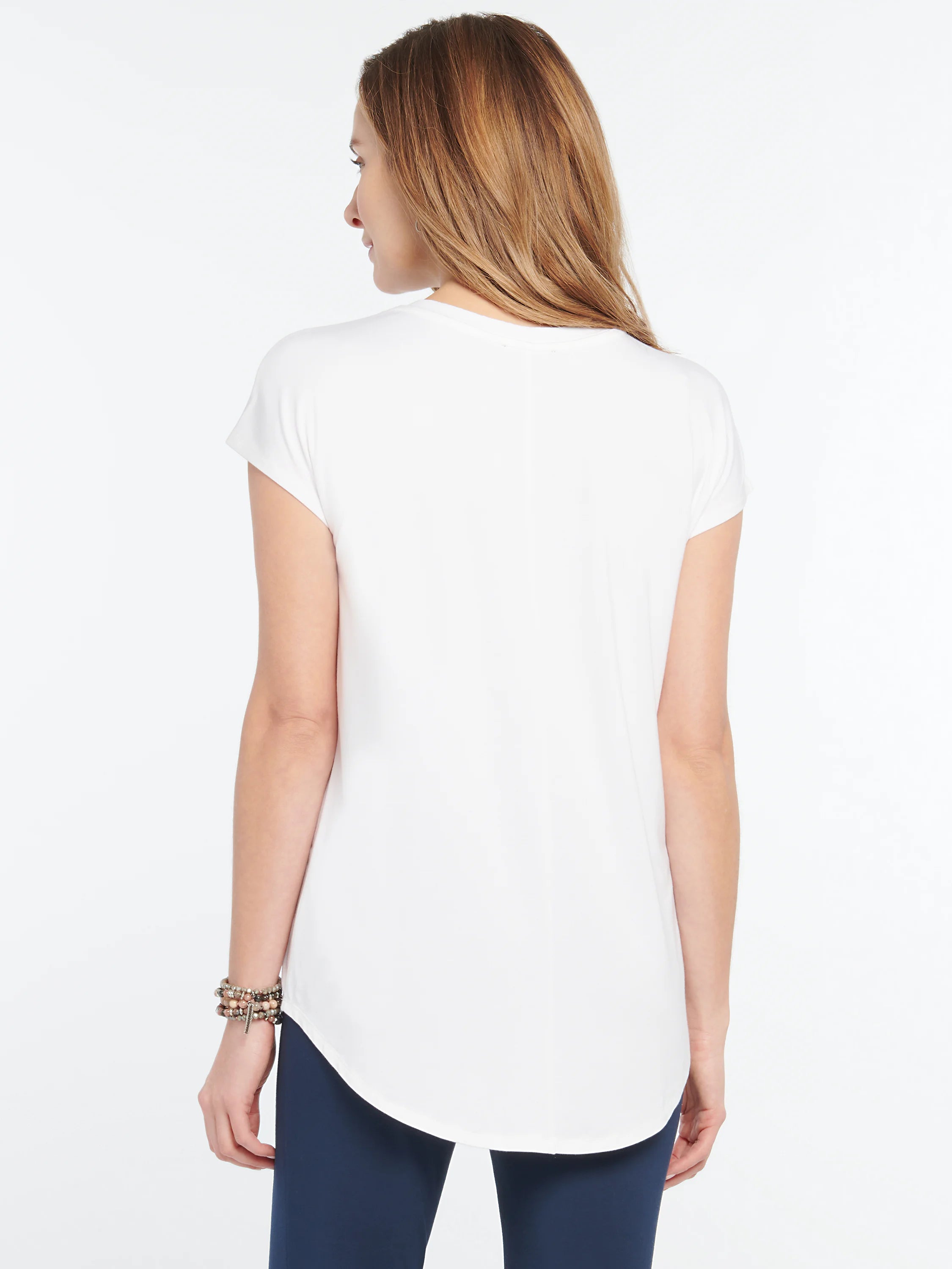White short-sleeved tee with a rounded hem, shown from the back on a model wearing dark blue pants.