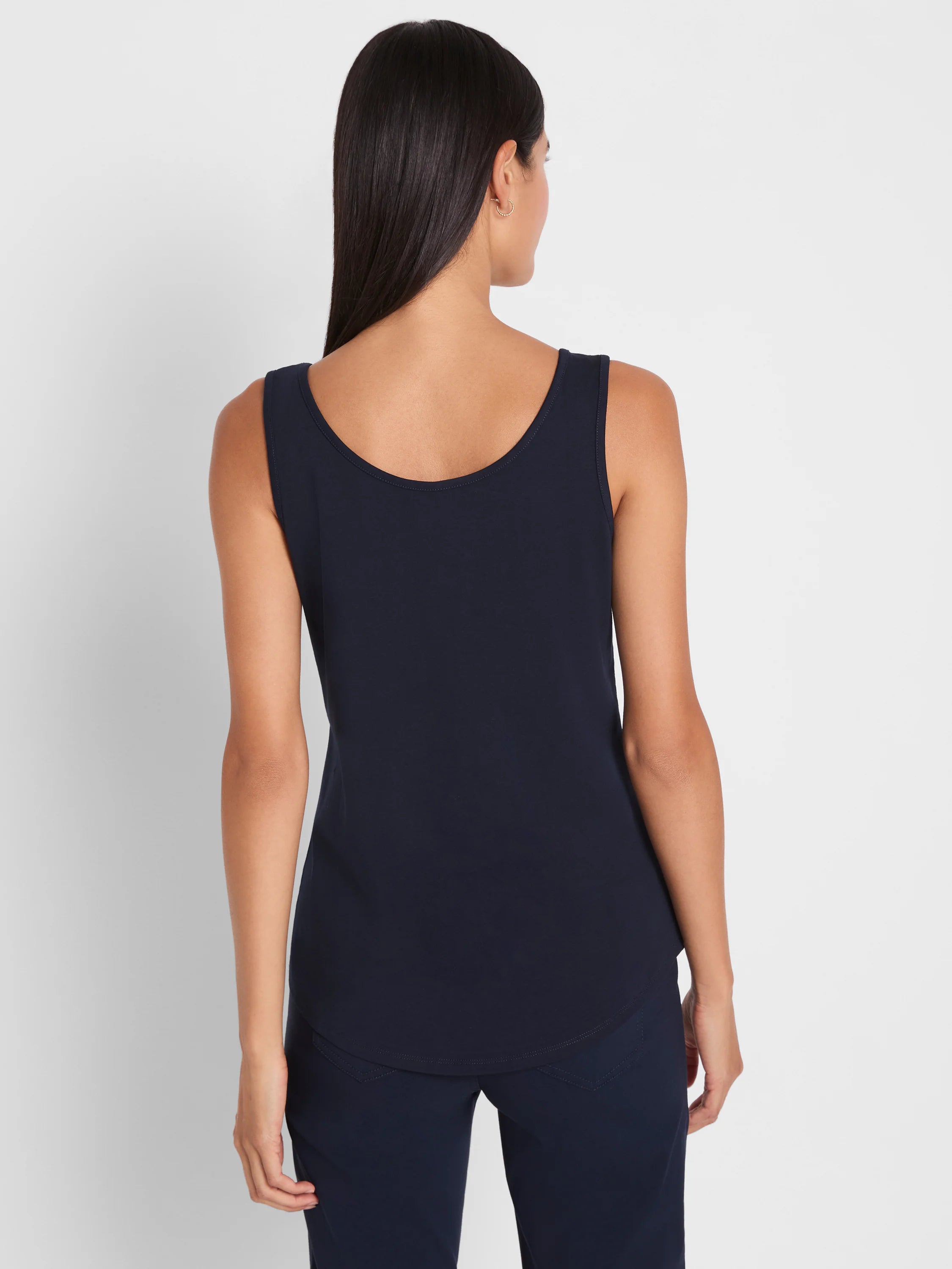 Navy sleeveless tank top with a scooped back and a curved shirt tail hem, worn by a model from the back.