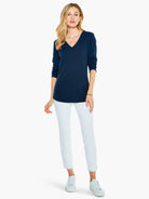 Navy blue, textured V-neck long-sleeve top.  Model is wearing white pants and shoes.