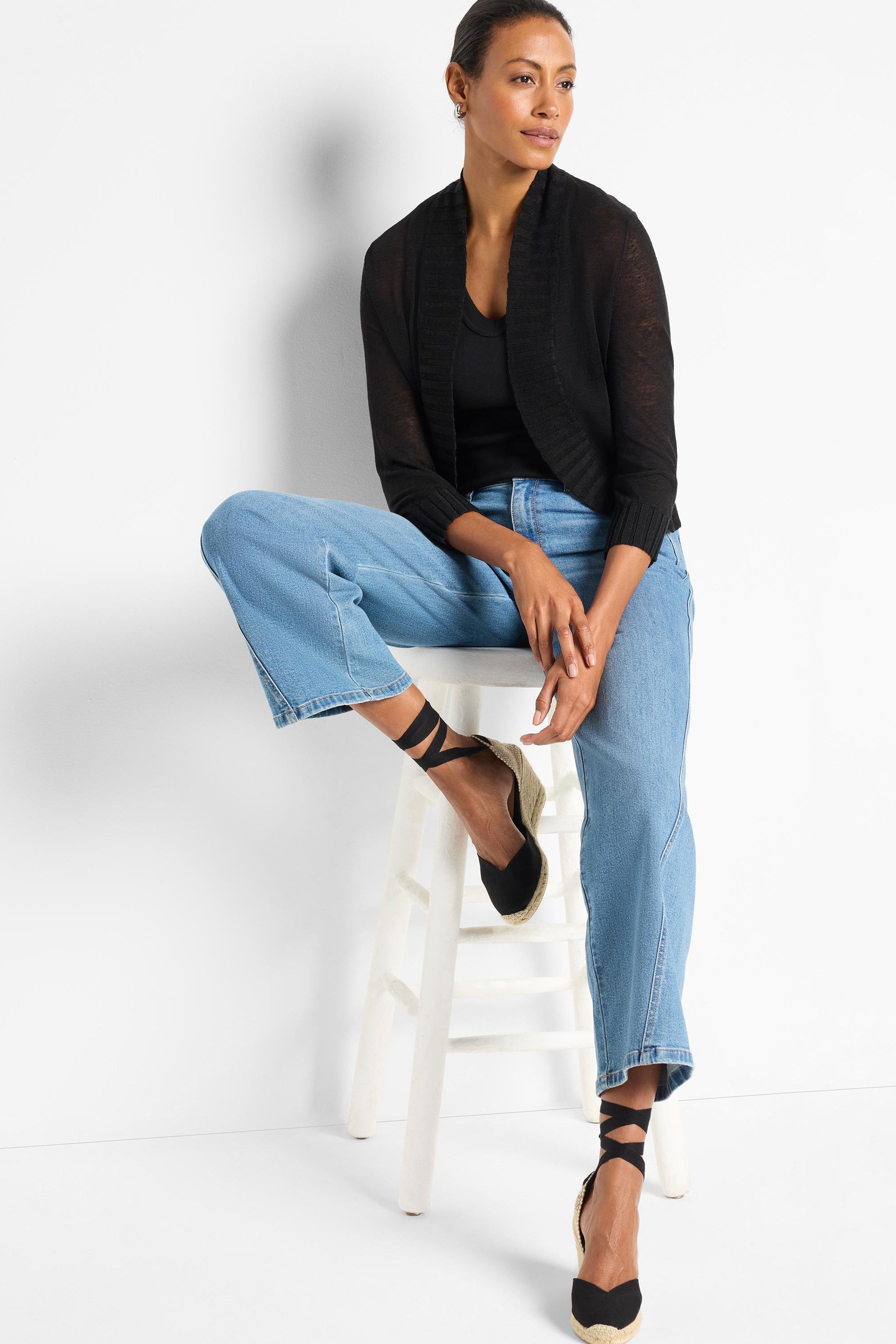 Black cropped knit bolero featuring sheer fabric, an open shawl front, and three-quarter length ribbed sleeves.