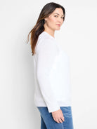 White lightweight cardigan with long sleeves and ribbed cuffs, paired with blue jeans.
