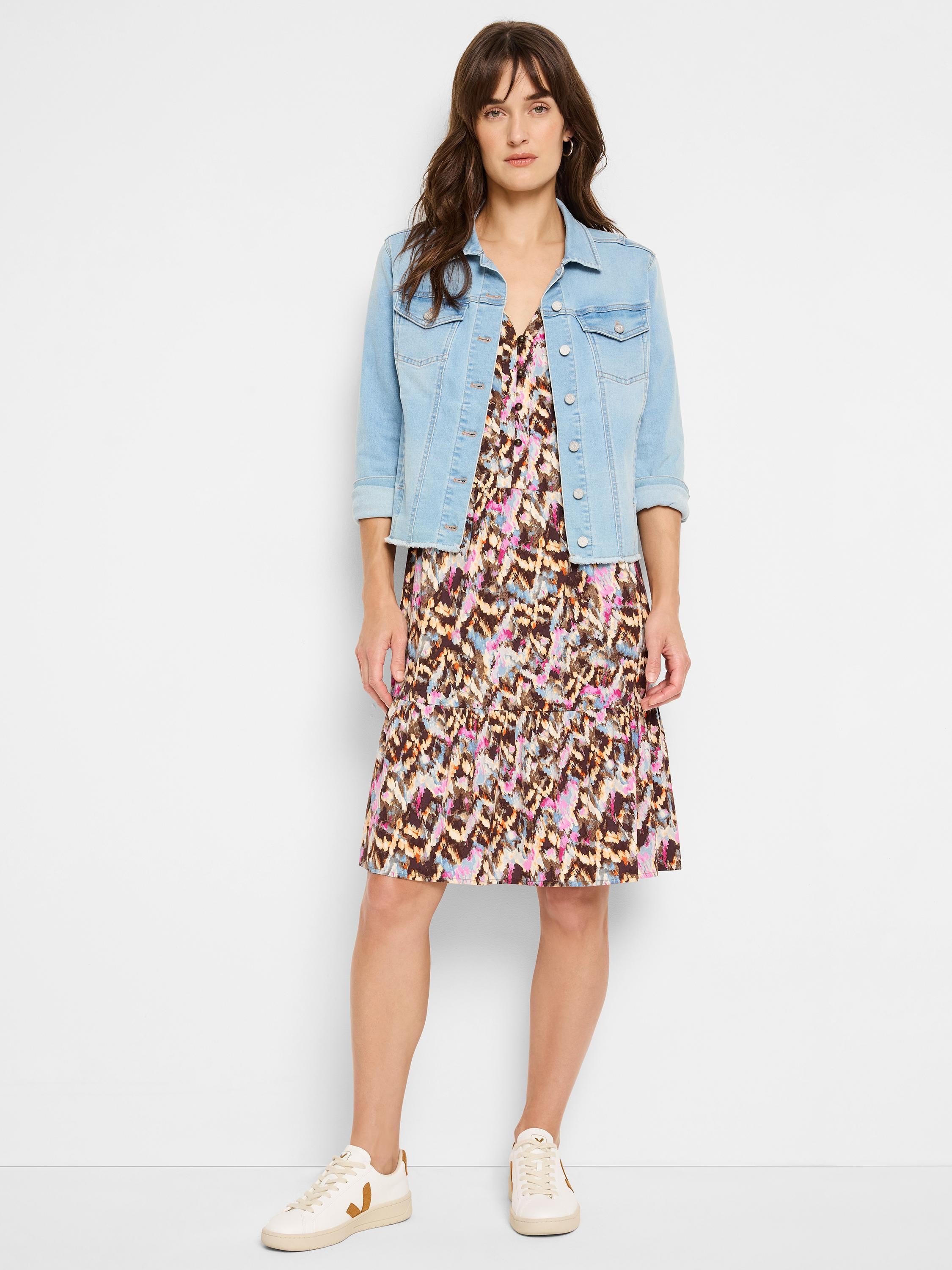 Cropped light wash denim jacket with a frayed hem is paired over a v-neck multicolored tiered print mini-dress.