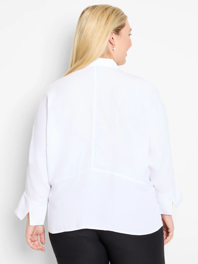White blouse, back view. Long cuffed sleeves, central back seam, and diagonal lower back seams. Model wears black pants.