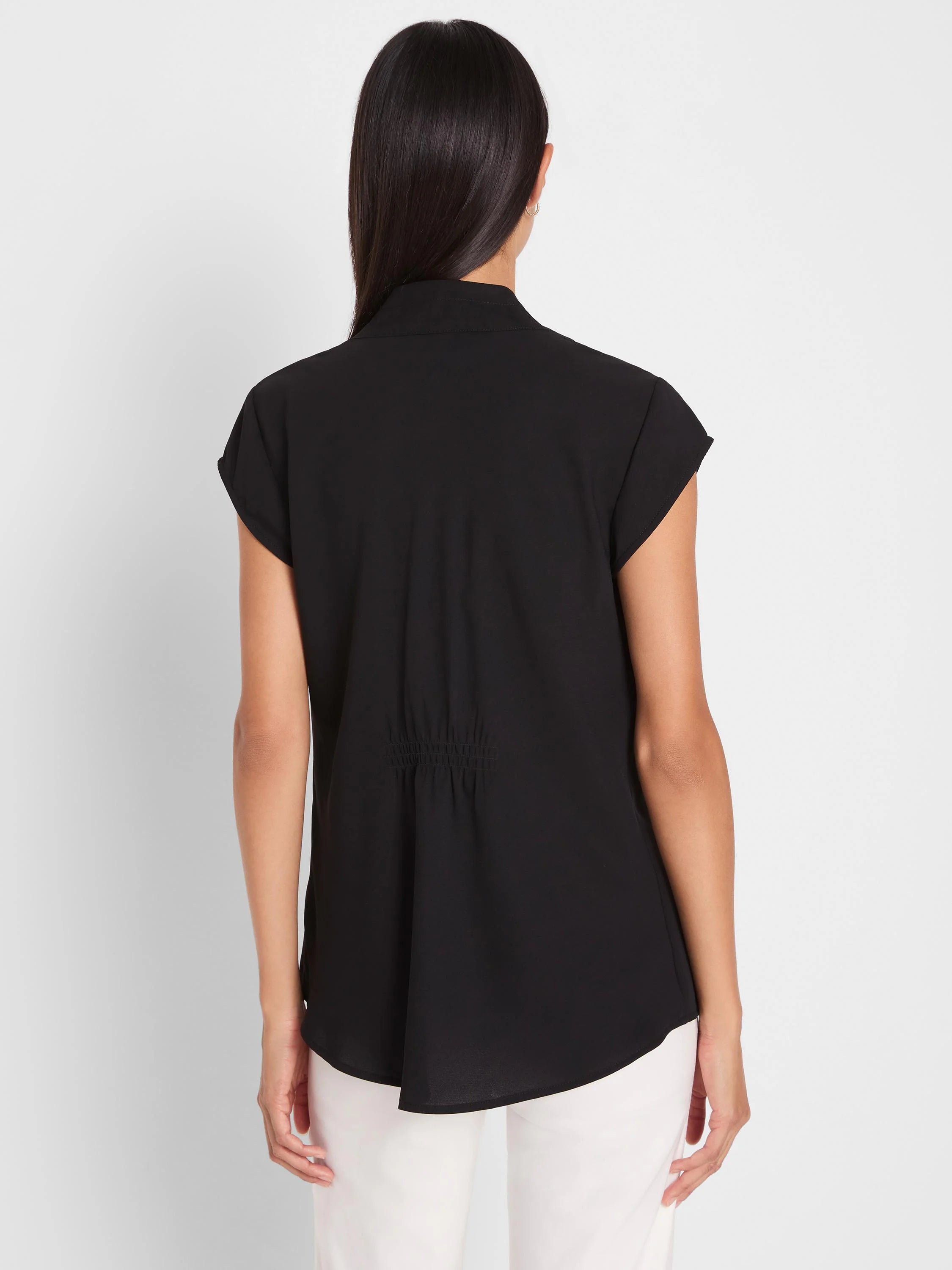 Black cap sleeve top, back view. Stand collar, smocked waist detail, and curved hem.