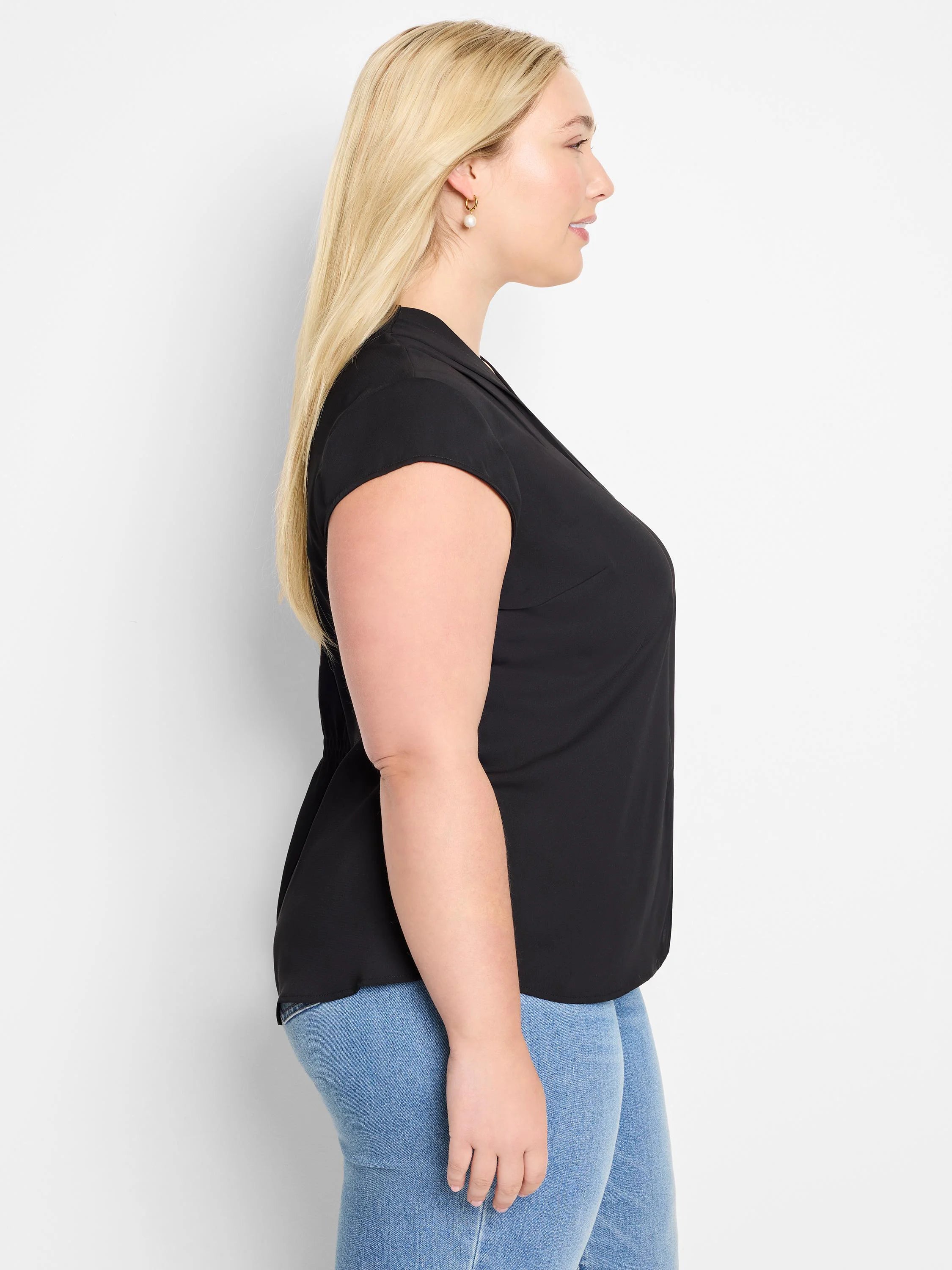 Black cap sleeve top with a notched V-neck and draped fit, shown on a model in profile.
